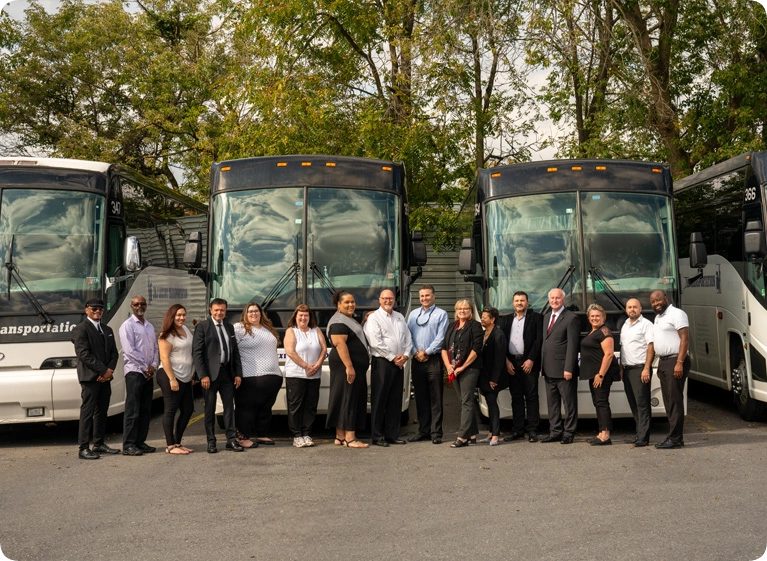 Four charter buses with people standing in front of them